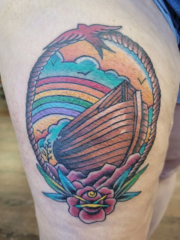 Colorful tattoo featuring a ship, rainbow, and flower design on the leg, showcasing vivid detail and shading.