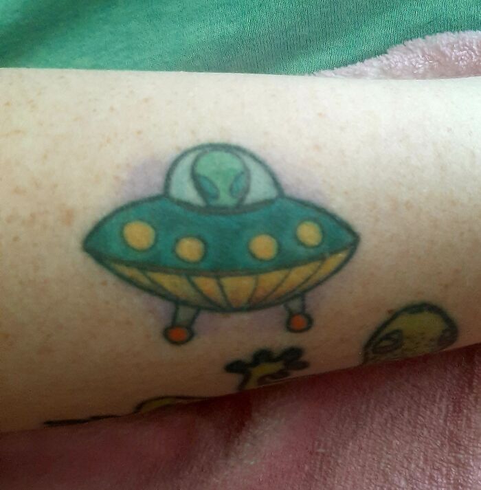 Colorful tattoo of a UFO with an alien on someone's arm.