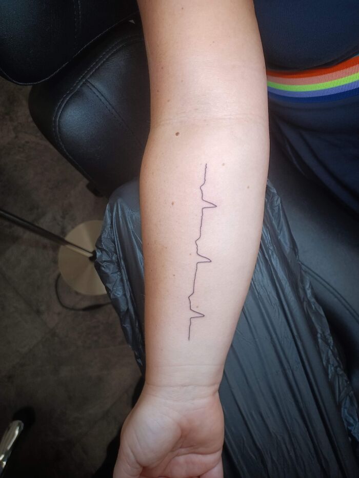Arm tattoo featuring a minimalist line design, resembling a heartbeat pattern.