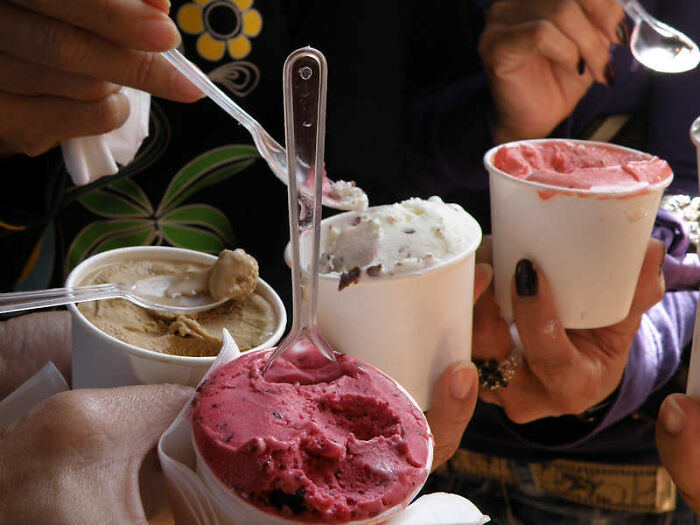 Four hands holding cups of colorful ice cream with spoons, illustrating casual moments guys should never say to partners.