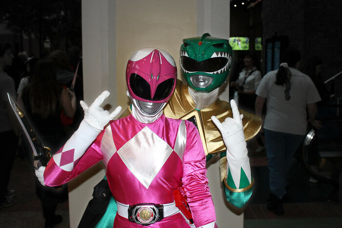Two people dressed as pink and green Power Rangers at a cosplay event, highlighting things guys should never say to partners.