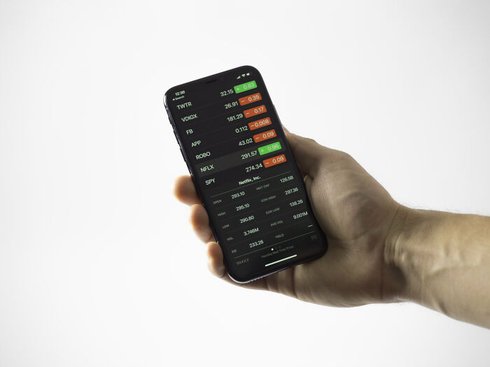 Hand holding smartphone displaying stock market app, illustrating things guys should never say to partners concept.