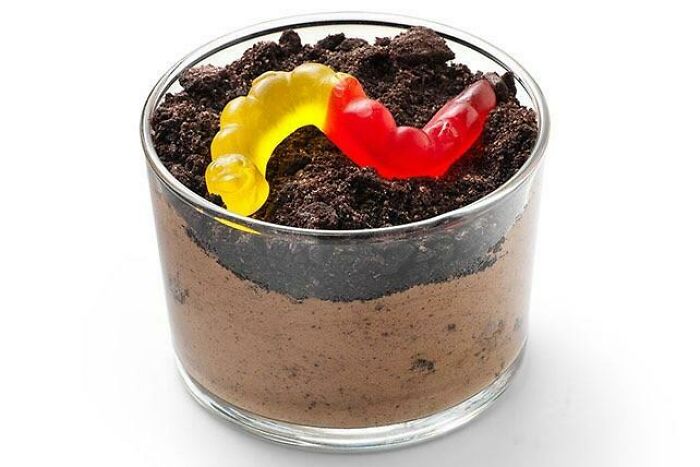 90s nostalgic food: a glass cup of chocolate pudding topped with crushed cookies and a gummy worm.