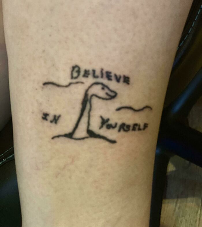 Poorly drawn tattoo of a dinosaur with text "Believe in yourself," showcasing a questionable tattoo choice.