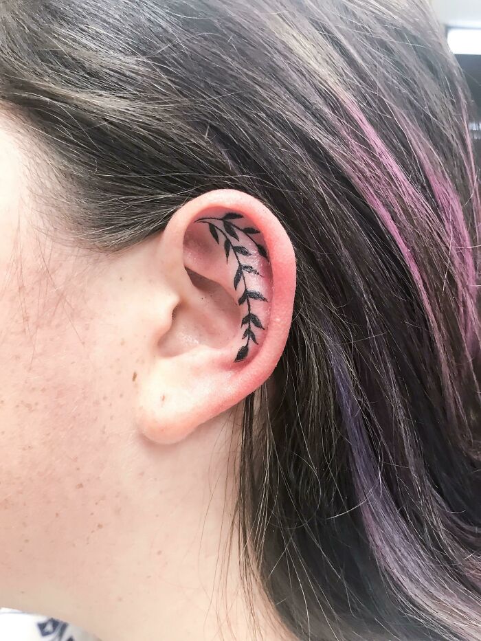 Leaf design ear tattoo on woman with brown hair.
