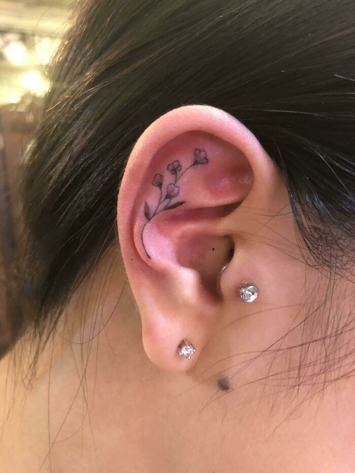 Delicate floral ear tattoo design with small buds and leaves behind the ear.