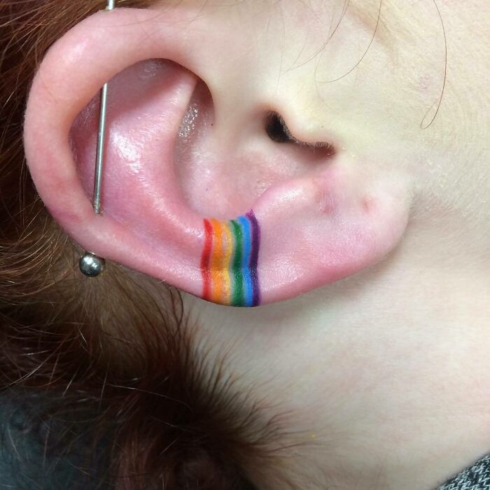 Close-up of an ear tattoo with a vibrant rainbow design along the inner fold.
