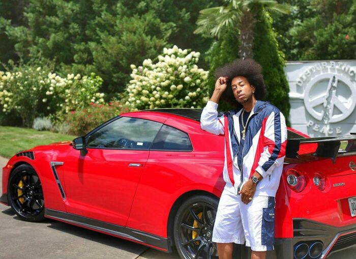 Celebrity posing with a luxurious red sports car in a lavish garden, exemplifying flaunting wealth.