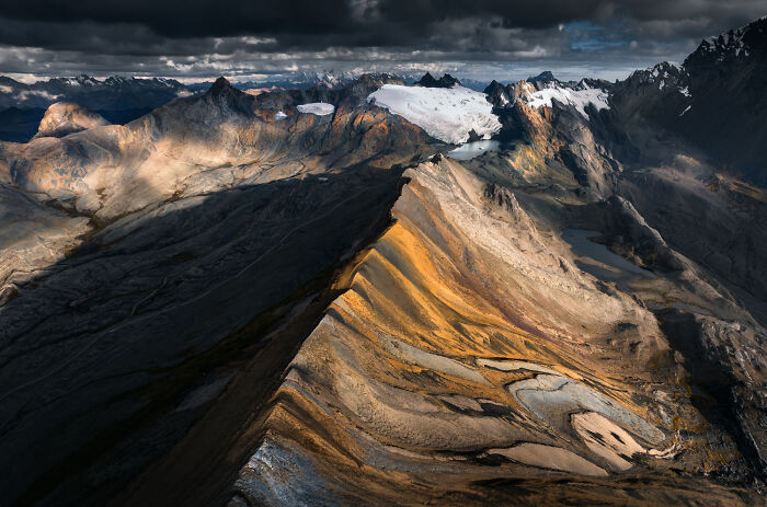 Dramatic view of the Peruvian Andes mountains with snow-capped peaks and rugged terrain under dark clouds.