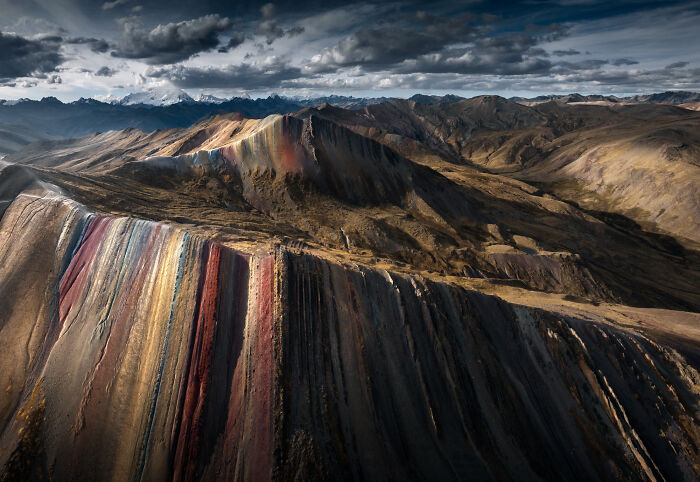 Colorful striped mountain formations in the Peruvian Andes under dramatic cloudy skies at sunset.