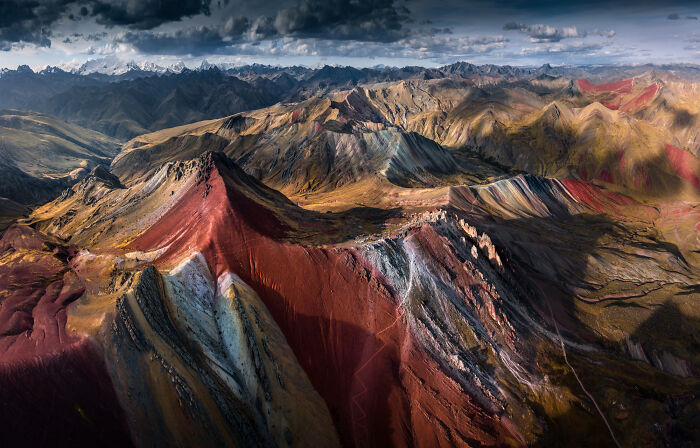 Aerial view of colorful mountains in the Peruvian Andes under dramatic cloudy sky during daylight.