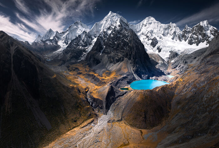 Snow-capped peaks and vibrant turquoise lake in the Peruvian Andes surrounded by rugged mountainous terrain under a dramatic sky.