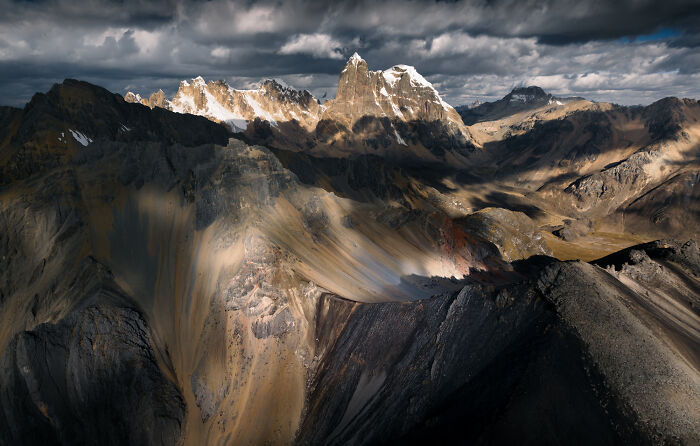 Dramatic Peruvian Andes mountain range with rugged peaks and sunlight breaking through dark stormy clouds.