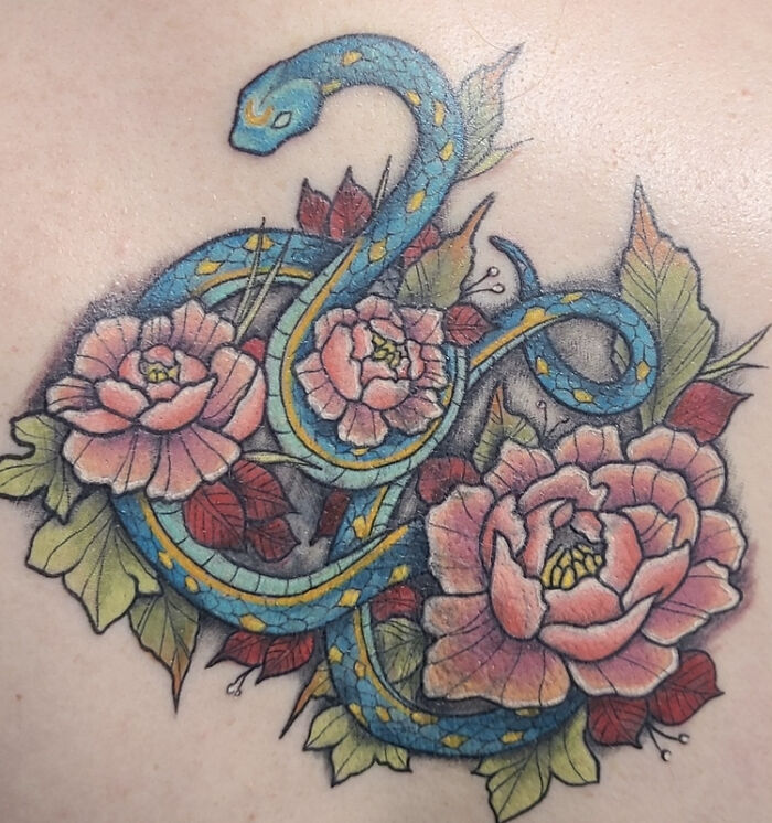 Colorful snake and peony flower tattoo on skin, featuring intricate blue and pink details.