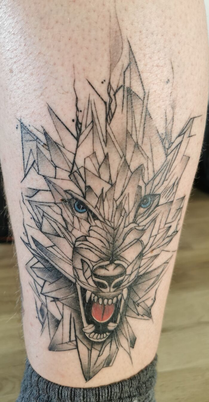 Geometric wolf tattoo with fierce eyes and open mouth on a person's leg, showcasing intricate line work and shading.