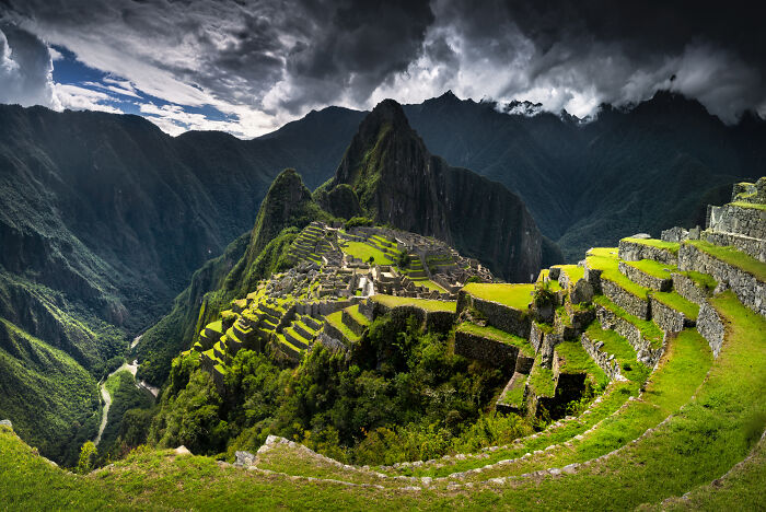 Ancient stone terraces and ruins of Machu Picchu in the Peruvian Andes under dramatic cloudy skies.