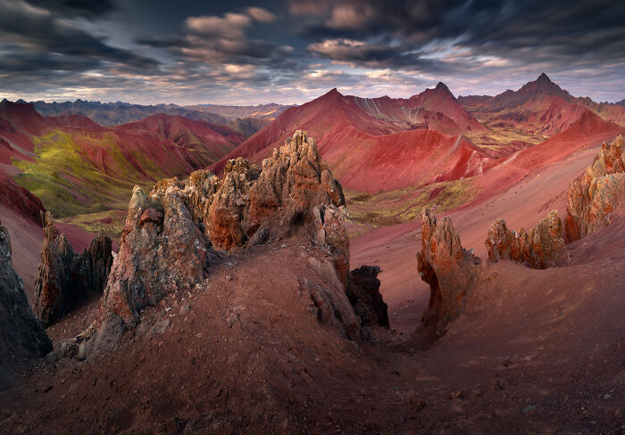 Colorful rocky peaks and ridges in the Peruvian Andes under a dramatic cloudy sky at sunset.