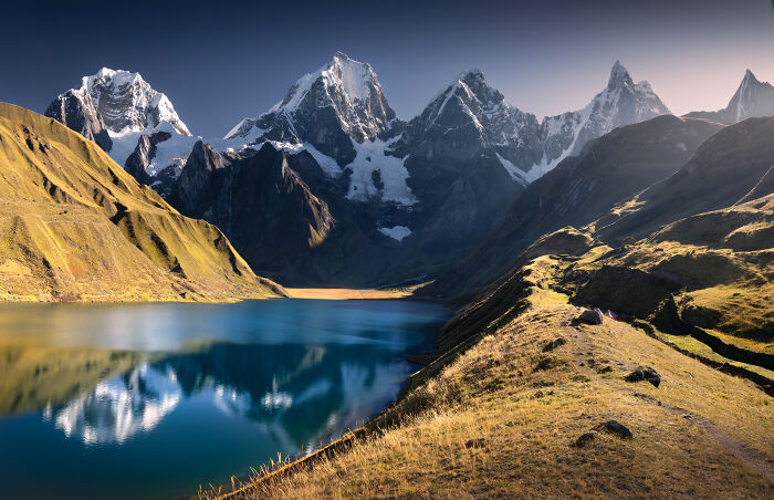 Scenic view of the Peruvian Andes with snow-capped peaks reflecting in a clear blue mountain lake at sunrise.