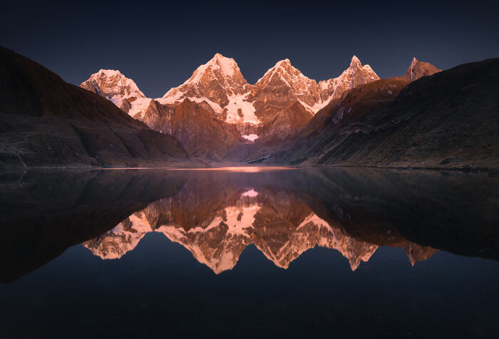 Snow-capped peaks of the Peruvian Andes bathed in golden light, reflected perfectly in a calm mountain lake at dawn.