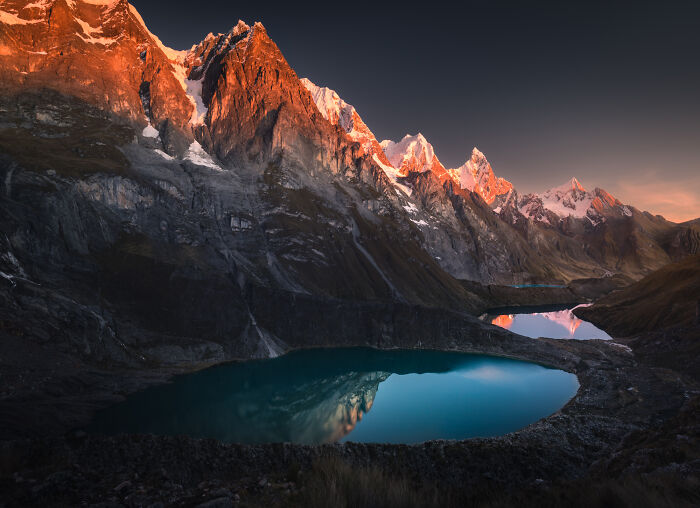 Sunset over snow-capped Peruvian Andes mountains with turquoise lakes reflecting rugged peaks and vibrant sky.