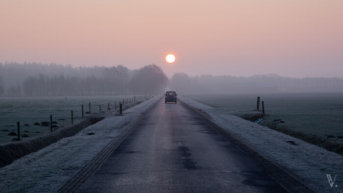 Car driving on a rural road at sunrise with fog and scenic countryside in the Netherlands landscape.