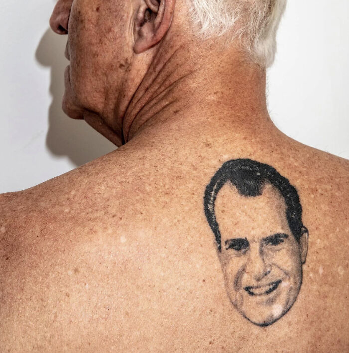 Back tattoo of a man's face on an older person's left shoulder, representing controversial tattoo choices.