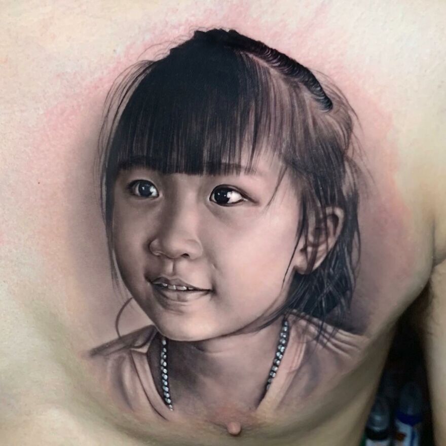 Hyper-realistic tattoo of a young girl with bangs, showcasing intricate detail and lifelike shading on the skin.