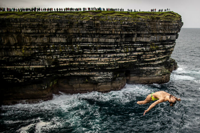 Cliff diver captured mid-air against ocean waves and rocky cliff, one of the best moments in sports photography 2022.
