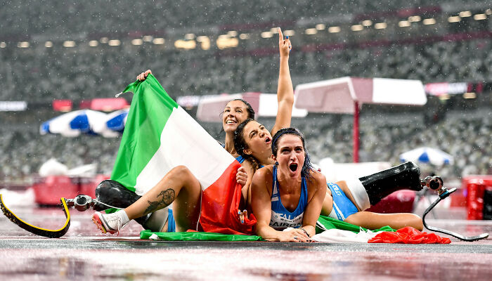Three athletes celebrating with an Italian flag on a rainy track, featured in best moments in sports photography.