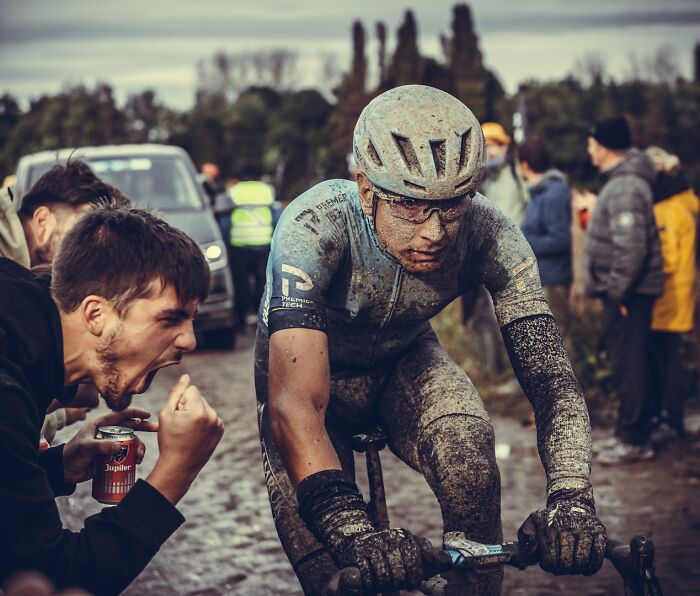 Cyclist covered in mud racing on a muddy trail while spectators cheer during a top sports moment in 2022.