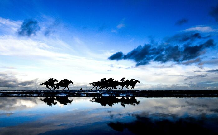 Silhouetted horse racing action captured with dramatic sky and water reflection, showcasing one of the best moments in sports photography.
