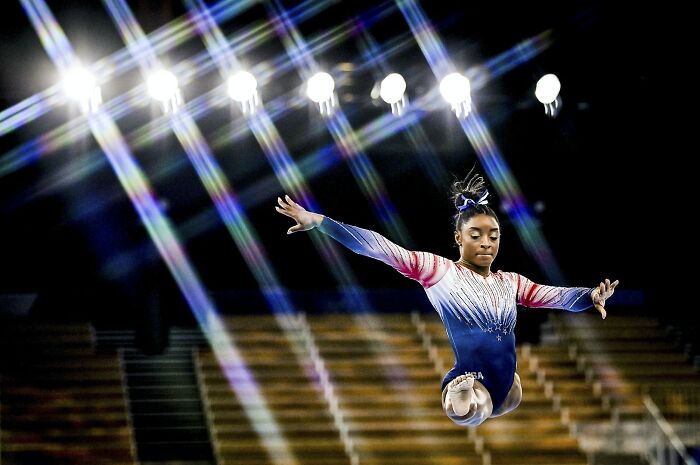 Gymnast performing a mid-air leap under bright lights, capturing one of the best moments in sports photography 2022.