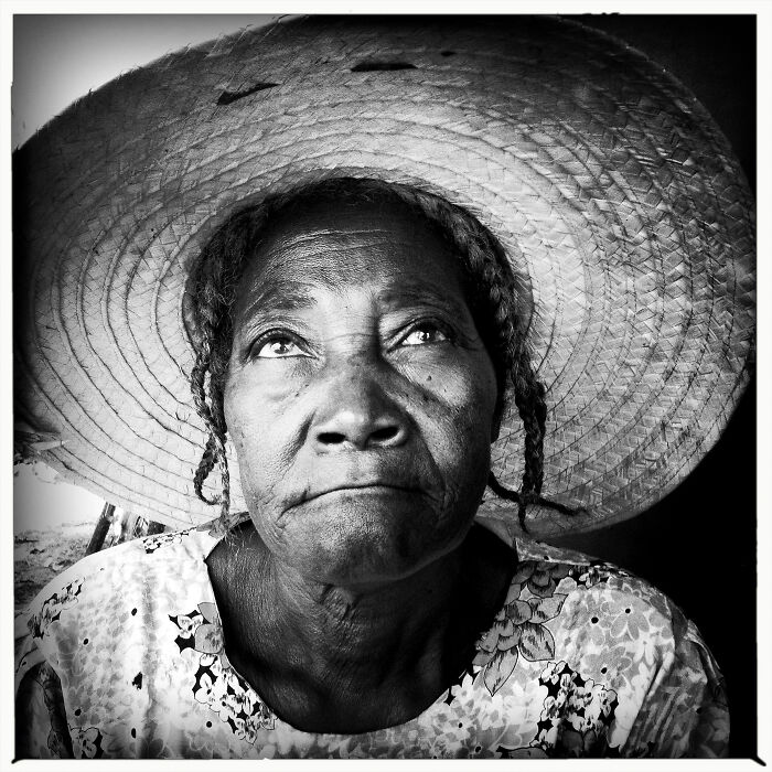 Black and white portrait of an elderly woman wearing a large hat, showcasing powerful portrait photography.