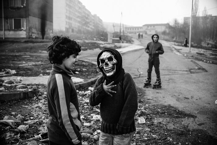 Black and white powerful portrait of children in urban setting with one wearing a skull mask captured by a photographer
