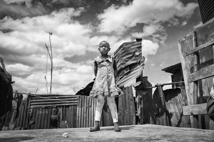 Black and white portrait of a young girl standing confidently in a rustic outdoor setting, powerful portrait photography.