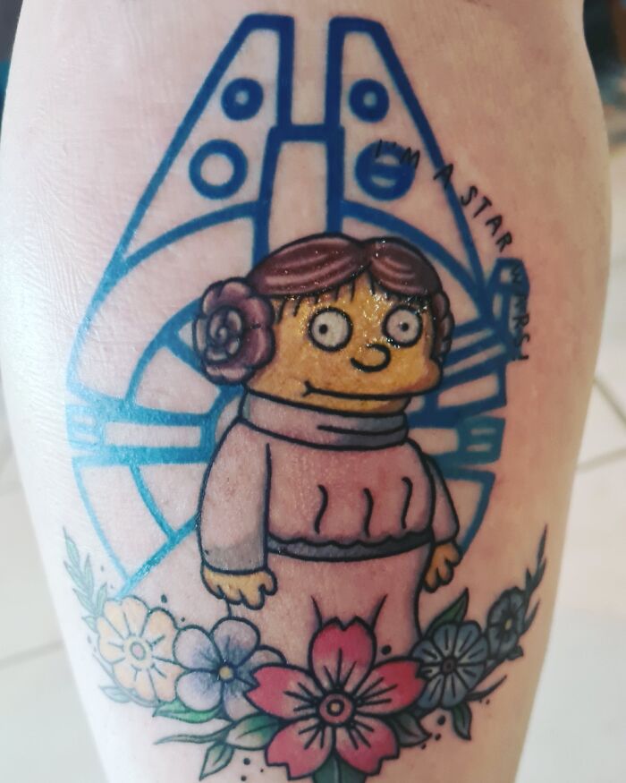 Cartoon-inspired tattoo with character in front of a spaceship and surrounded by colorful flowers.