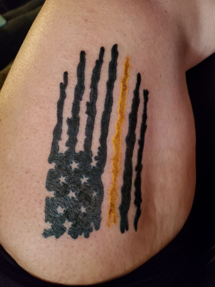Tattoo featuring a stylized American flag design with black and yellow stripes on shoulder.