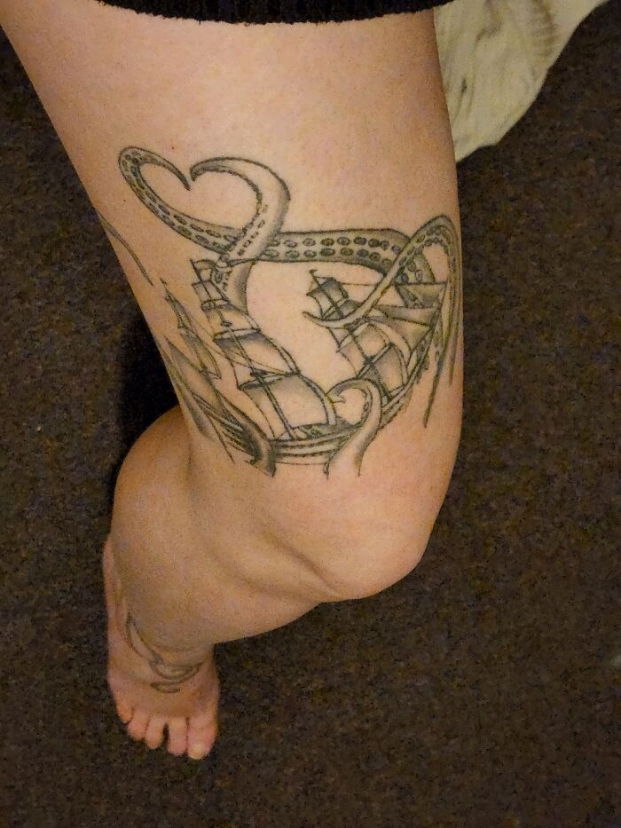 Tattoo of a ship and tentacles on a person's leg.