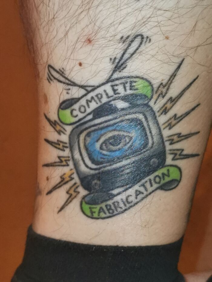 Tattoo of a TV with an eye, surrounded by lightning bolts, featuring the words "Complete Fabrication."