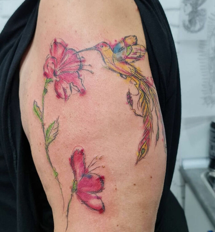 Colorful hummingbird and flower tattoo on an arm, showcasing detailed ink artistry.