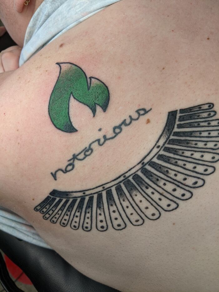 Tattoo of a green flame and "notorious" text with a black pattern on skin.