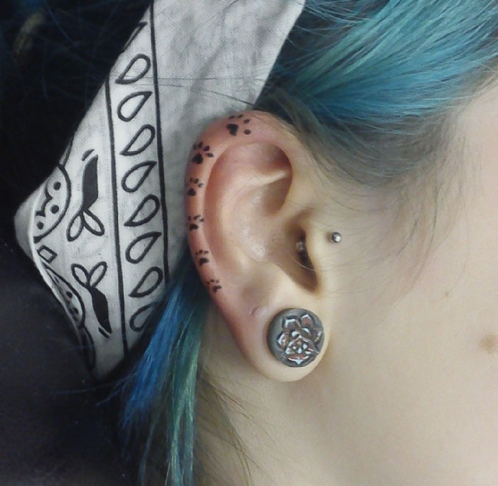 Ear tattoo with paw print design and decorative earring.
