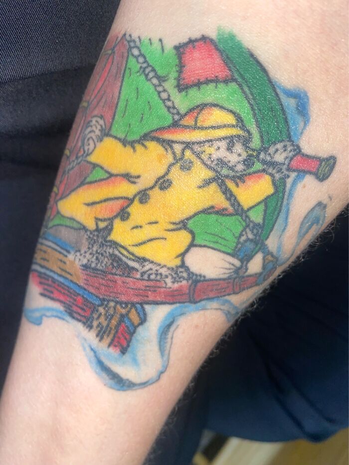 Colorful tattoo of a character in a yellow raincoat, featuring vibrant red, green, and blue background elements.