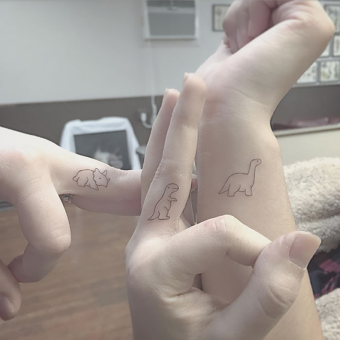 Minimal tattoo designs featuring small dinosaur outlines on fingers and wrists.
