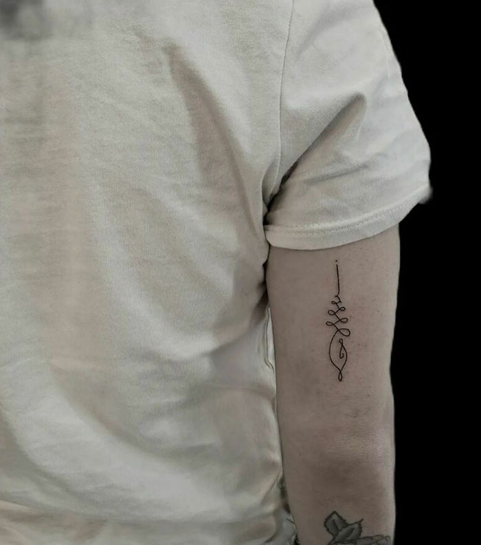 Minimalism line tattoo on upper arm of person in a beige shirt.