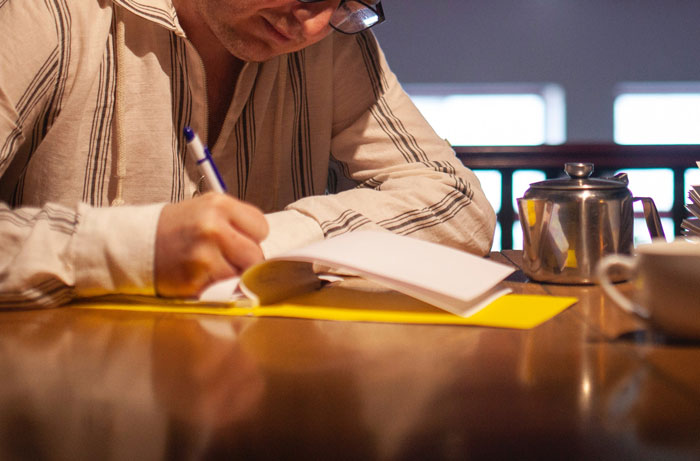Person writing in a notebook at a table, illustrating entertaining it doesn’t work like that stories shared by professionals.
