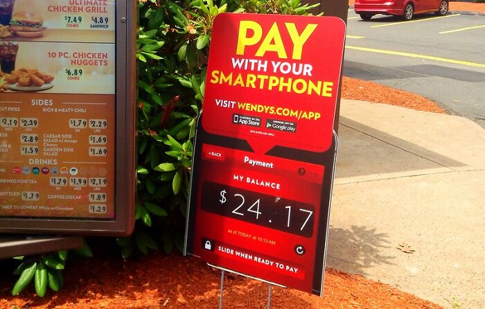 Sign at fast food restaurant advertising smartphone payment option, highlighting digital convenience and potential crime risks online.