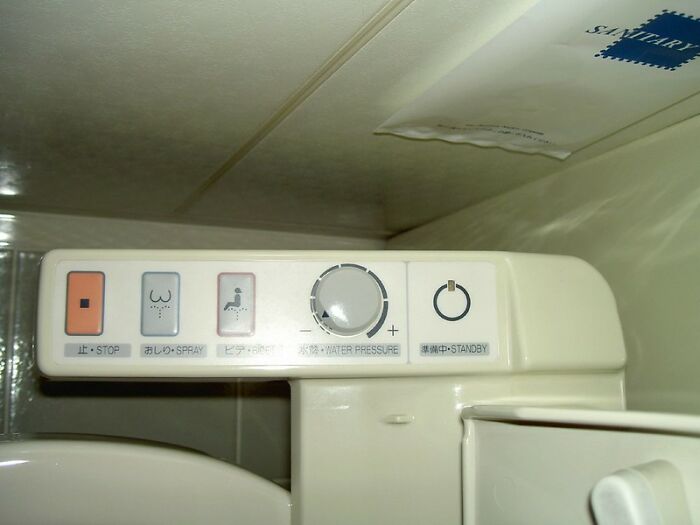Control panel of a Japanese toilet bidet showing water pressure dial and spray options, related to committing a crime.