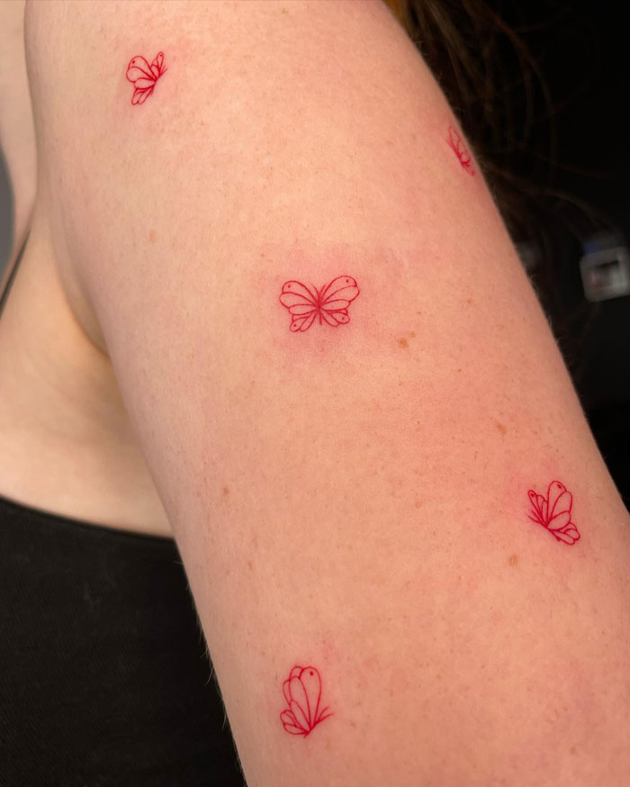 Red butterfly minimal tattoos on an arm.