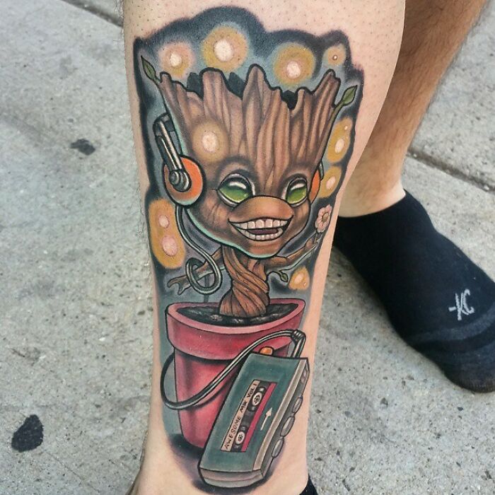 Marvel tattoo featuring Baby Groot wearing headphones, potted with a retro cassette tape, on a person's leg.